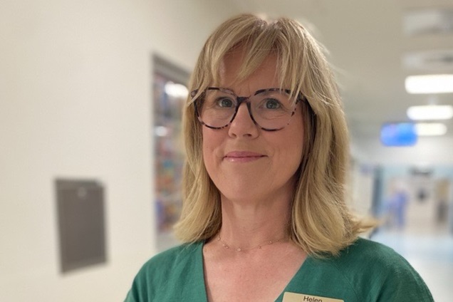 A smiling woman wearing a green dress and glasses.