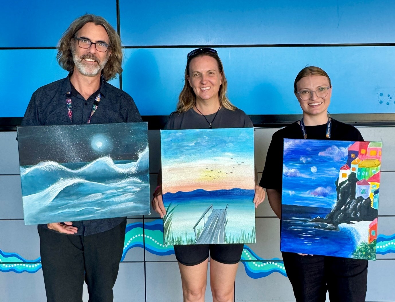 Three people holding artwork showcasing work from young artists